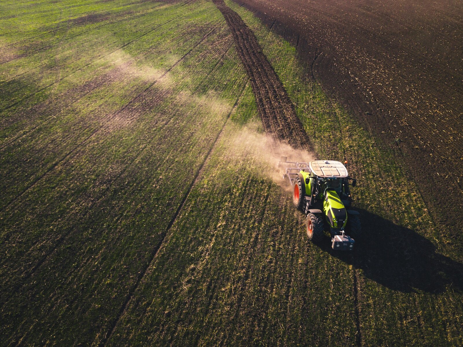 Tractor applying fertiliser across a field, aerial view